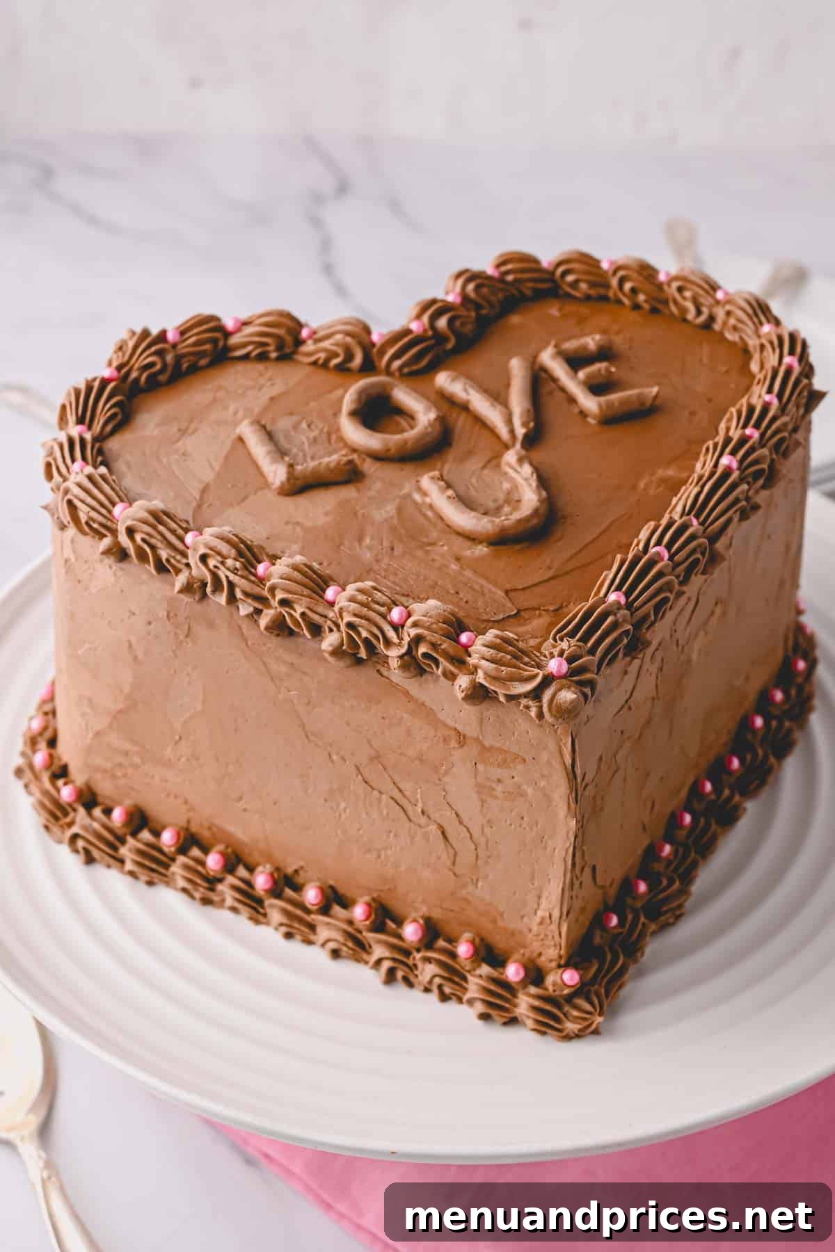 A fully decorated chocolate heart cake on a plate, adorned with chocolate buttercream, festive pink sprinkles, and the sweet message "love u" piped on top.