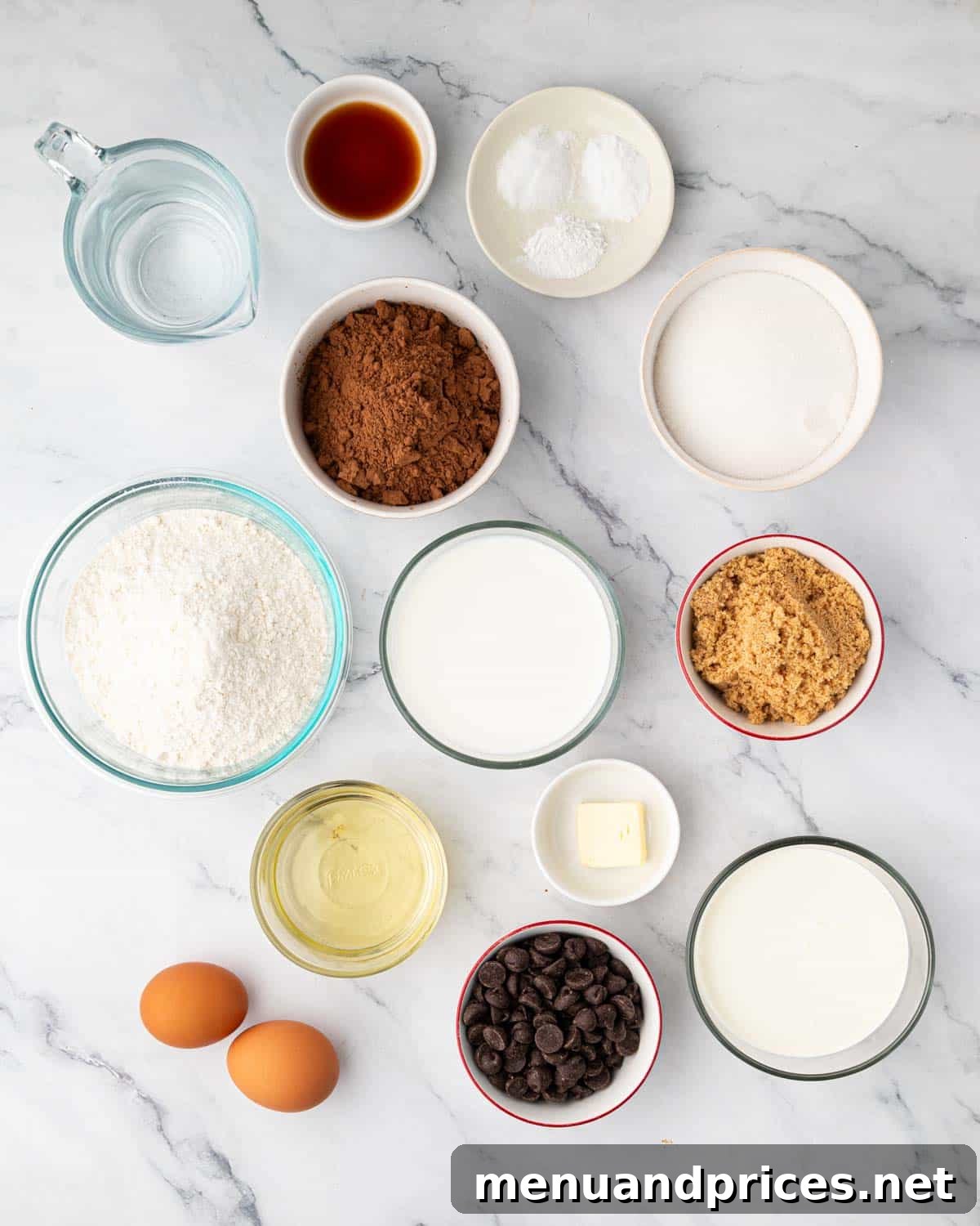A selection of key ingredients laid out for making a chocolate heart cake, including cocoa powder, flour, sugar, butter, and chocolate.