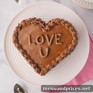 A chocolate heart cake on a plate with chocolate meringue icing and words piped that say "love u".