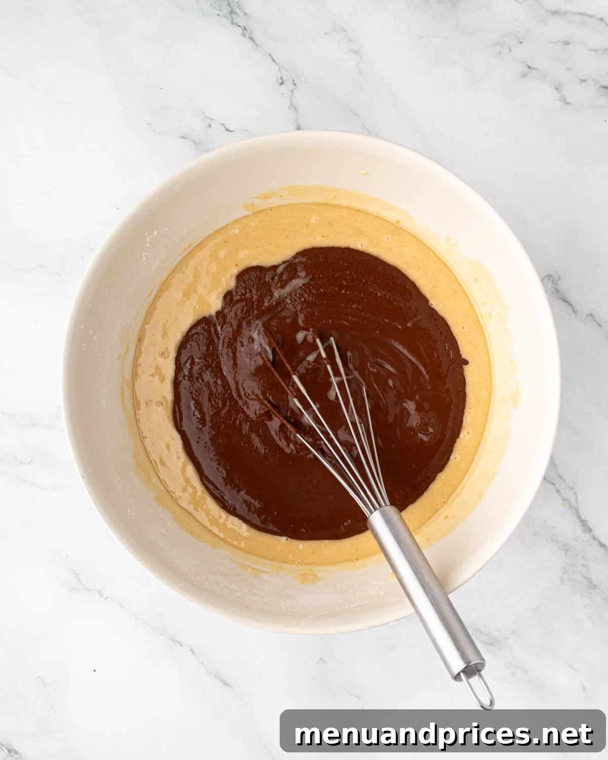 Wet ingredients for chocolate cake batter being whisked in a bowl.