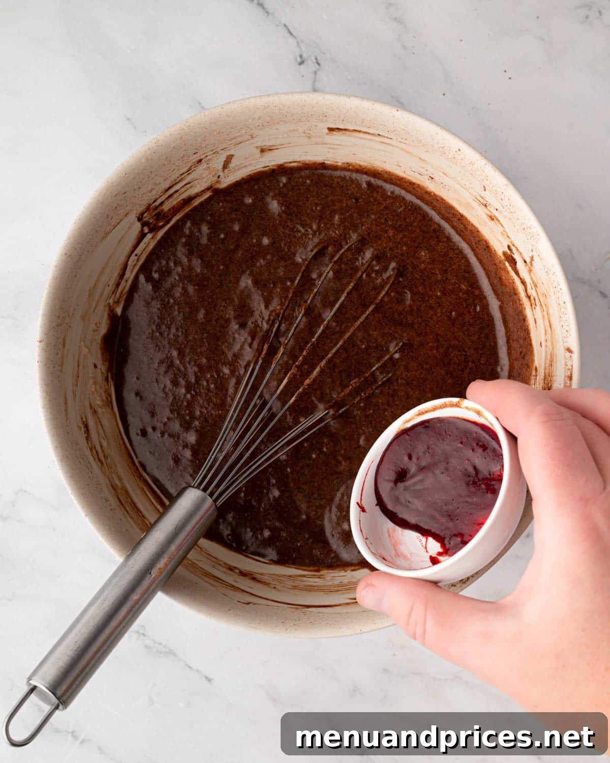 Crimson Velvet Brownies 11 Red gel food coloring being added to a bowl of red velvet brownie batter, with a whisk still in the bowl.
