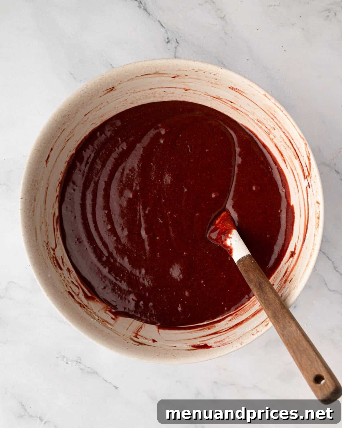 Crimson Velvet Brownies 12 A bowl of fully mixed red velvet brownie batter with a rubber spatula, showing its consistent red color and smooth texture.