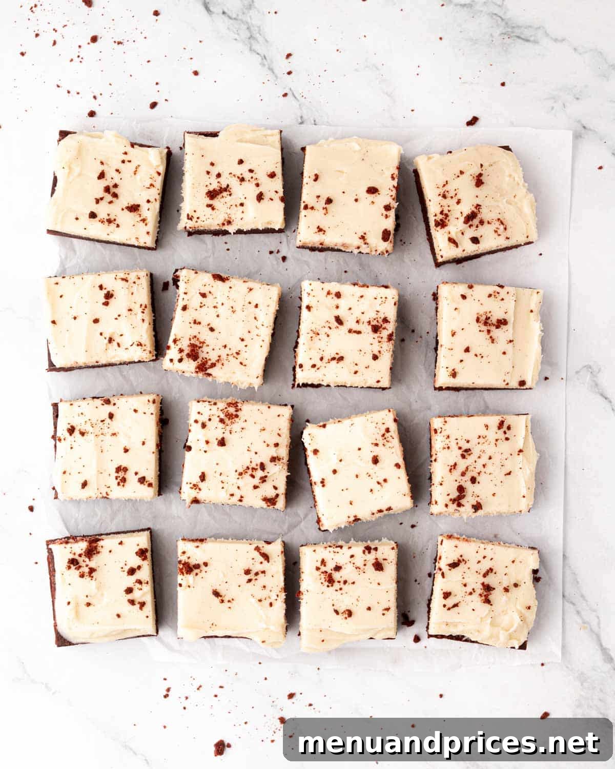 Crimson Velvet Brownies 19 Perfectly sliced red velvet brownie squares, each with a generous dollop of cream cheese frosting, arranged on parchment paper.