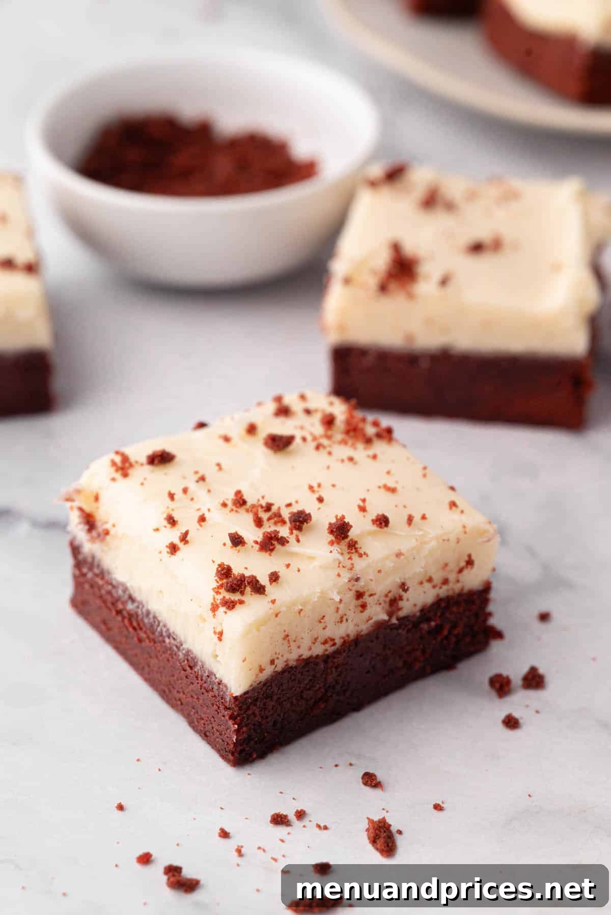 Crimson Velvet Brownies 20 Two perfectly cut red velvet brownies, each adorned with a generous swirl of cream cheese frosting.