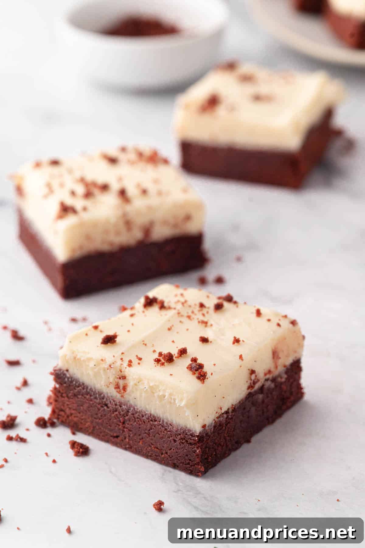 Crimson Velvet Brownies 3 Three red velvet cake brownies topped with a swirl of cream cheese frosting, presented beautifully.