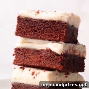 A stack of three red velvet brownies with cream cheese frosting on a plate.