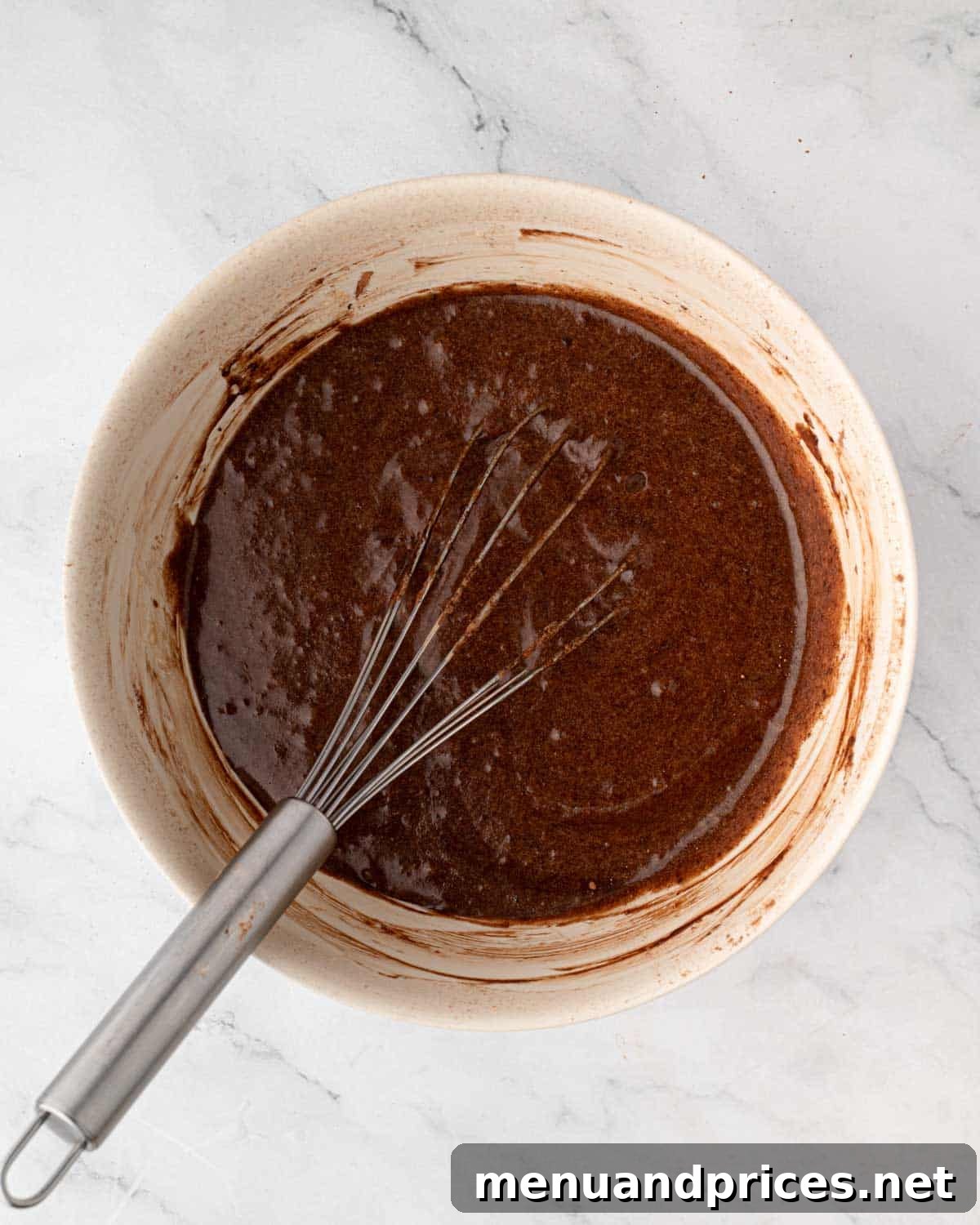 Crimson Velvet Brownies 10 Red velvet brownie batter in a mixing bowl with a whisk, showing the smooth, chocolatey texture after cocoa powder has been incorporated.