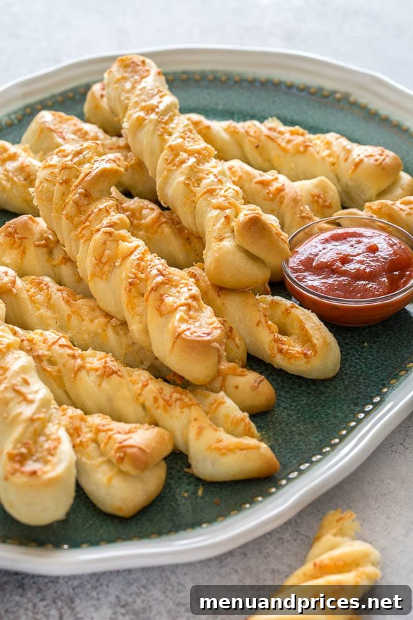 A close-up shot of golden brown roasted garlic and cheese breadsticks, twisted and perfectly baked, resting on a baking sheet with parchment paper.