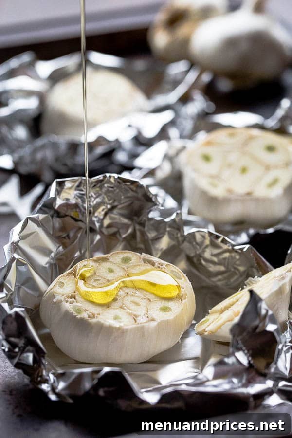 A close-up of a head of garlic, sliced horizontally to expose the cloves, generously drizzled with olive oil, prepared for roasting.