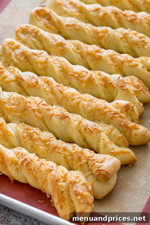 A close-up view of multiple perfectly baked, golden brown roasted garlic and cheese breadsticks, showcasing their appealing twisted texture and bubbling melted cheese.