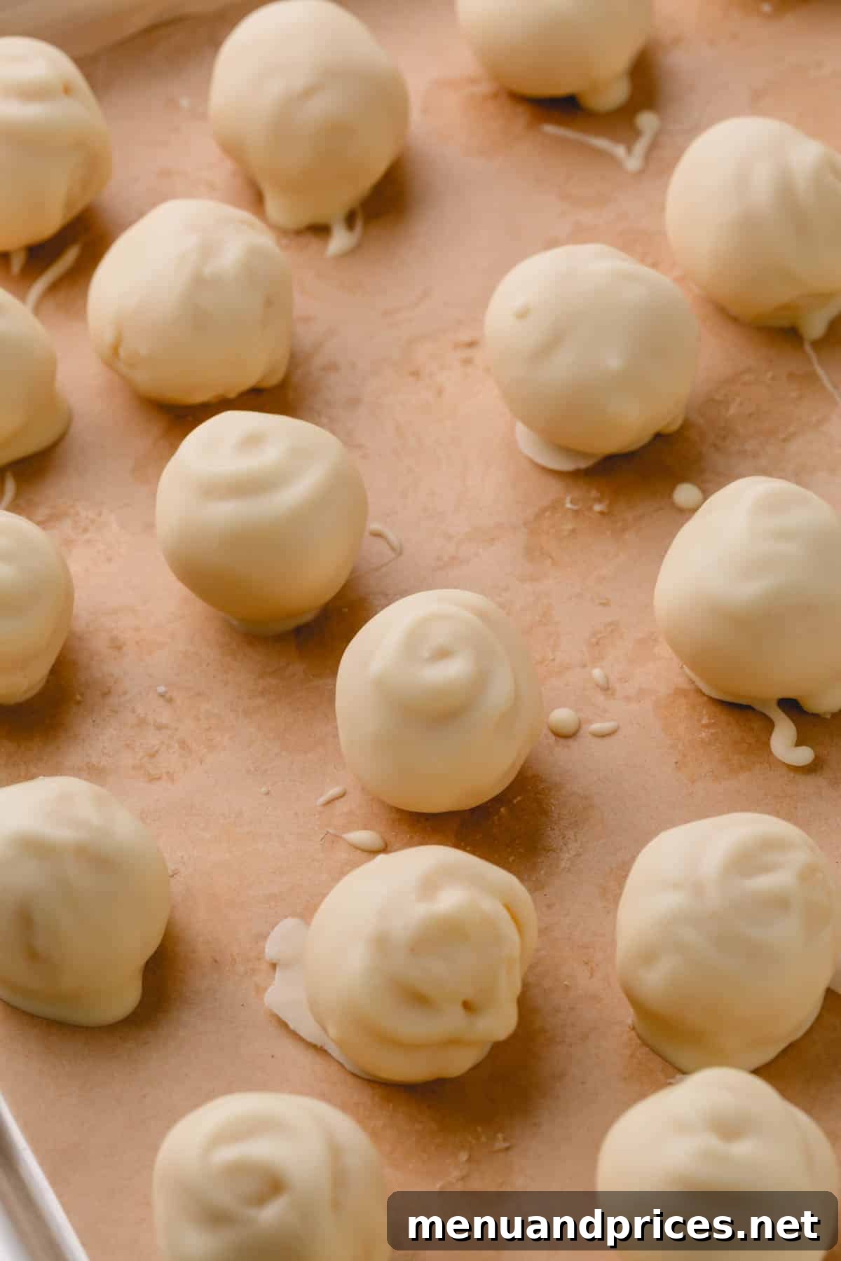 Almond Coconut Delights 14 White chocolate covered coconut balls on a parchment paper-lined baking sheet.