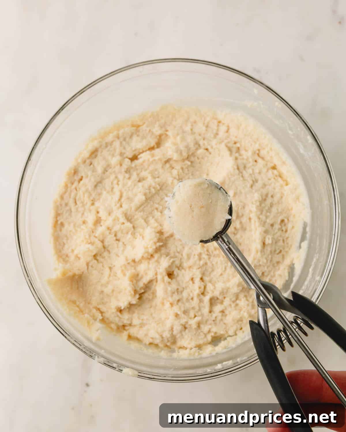 Almond Coconut Delights 9 A bowl of almond coconut balls batter with a cookie scoop full of dough held above it.