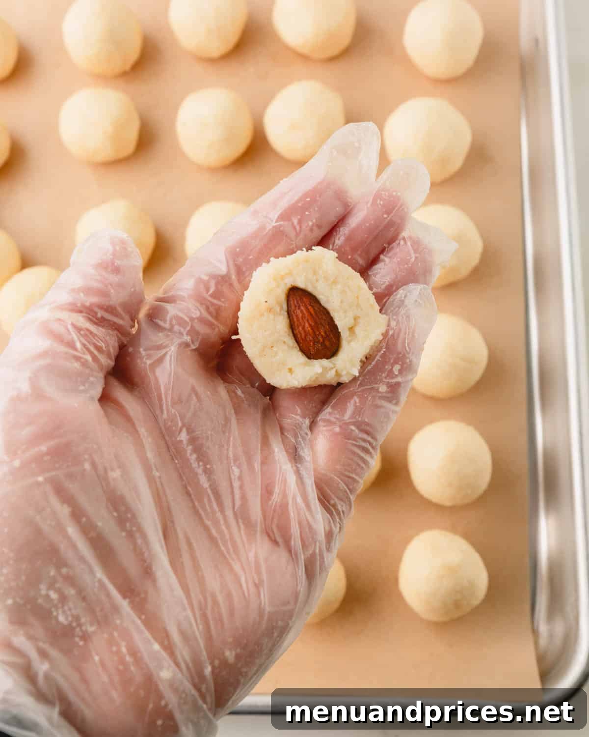 Almond Coconut Delights 10 A hand holding a coconut ball with a hole pecan in the center above a sheet tray of almond coconut balls.