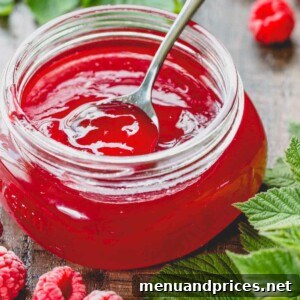 A glass jar of raspberry jelly with a spoon dip in it.