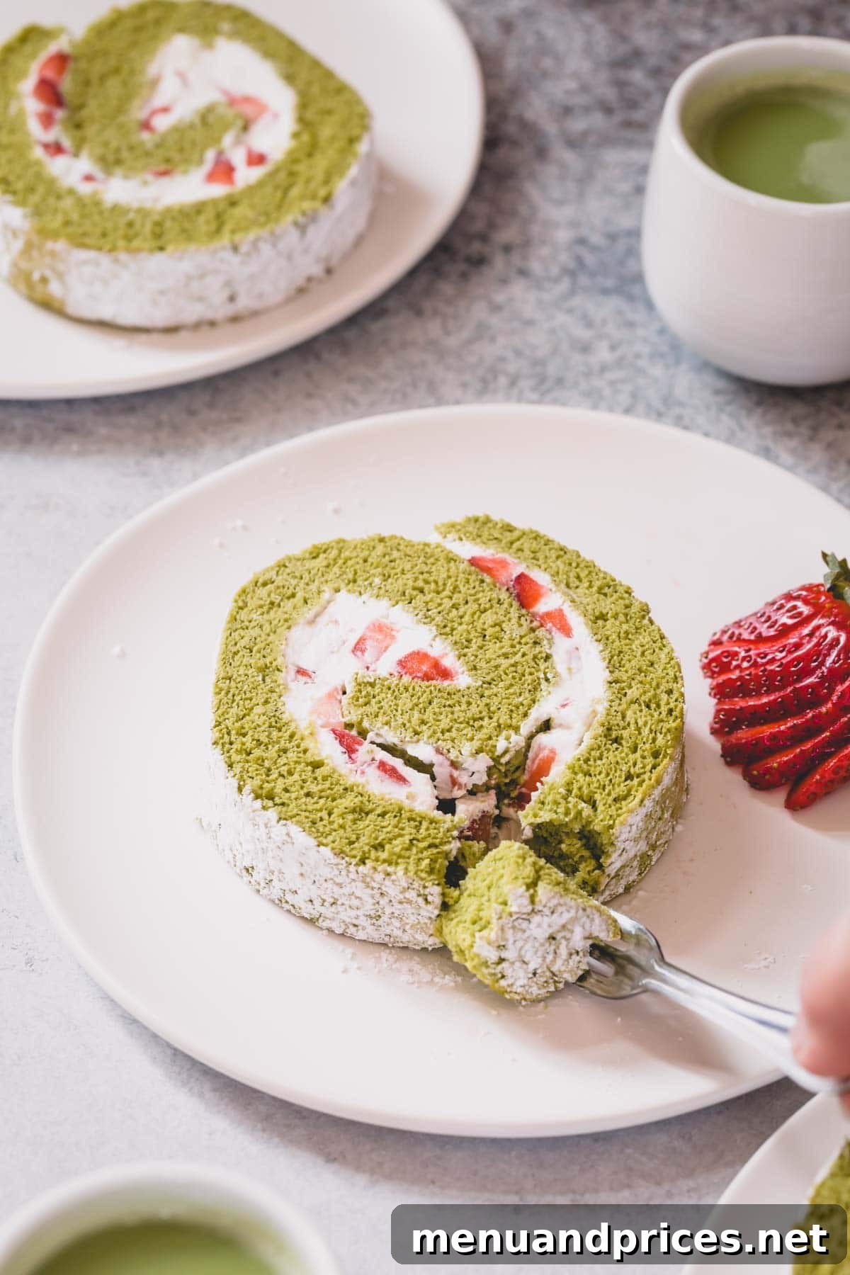 A perfectly sliced strawberry matcha roll cake on a white plate with a fork taking a bite.