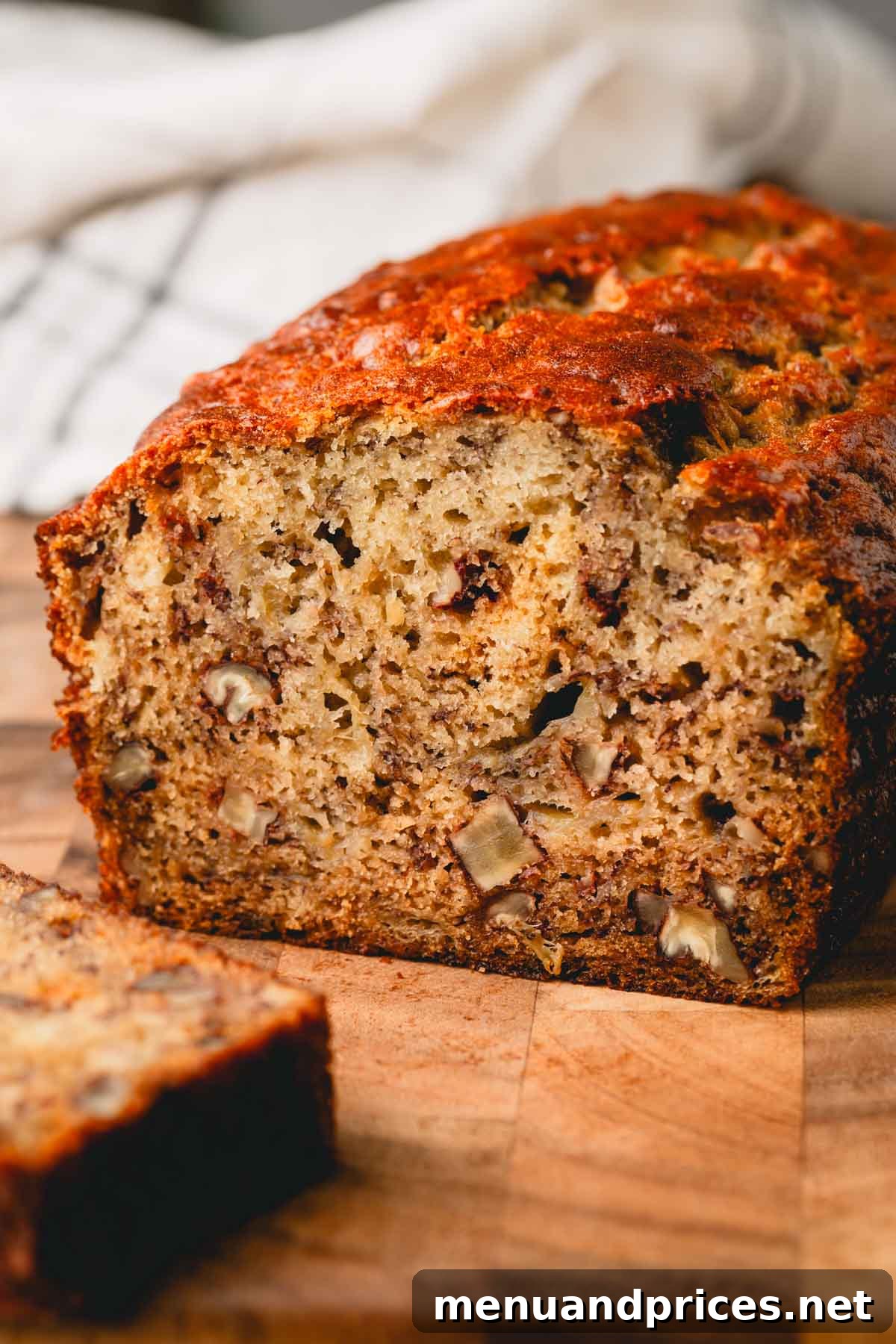 A beautifully sliced loaf of banana bread, revealing its moist, tender interior studded with nuts, alongside an unsliced loaf.