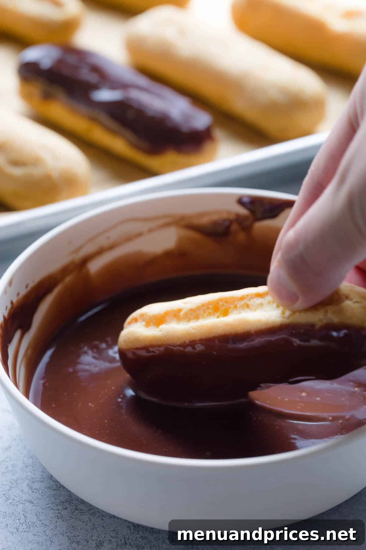 Divine Chocolate Eclairs 12 A filled éclair being dipped into a bowl of smooth chocolate ganache.