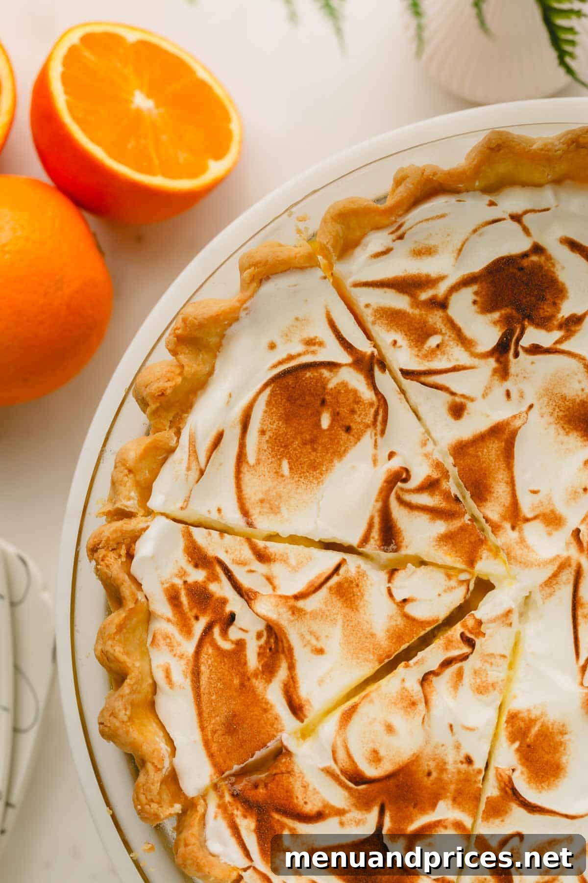 Zesty Orange Cloud Pie 12 An elegantly presented orange meringue pie, with several slices removed, on a platter alongside fresh orange halves.