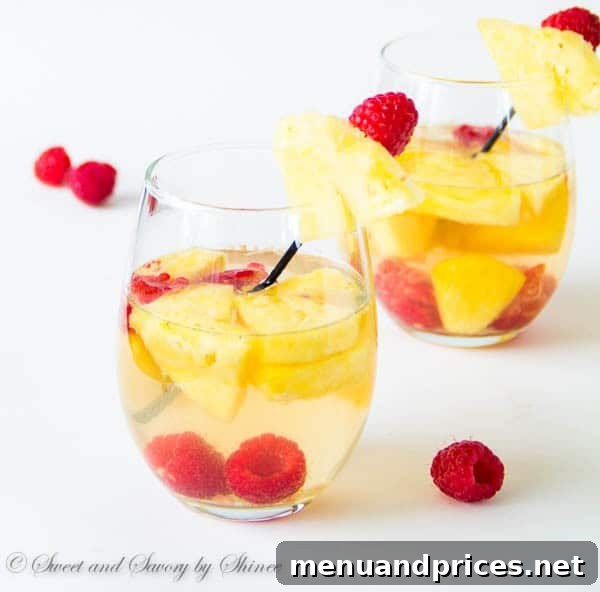 Two glasses of Pineapple Raspberry Sangria next to a pitcher