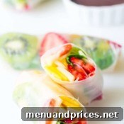 Prepared fruit spring rolls on a plate with dipping sauces.