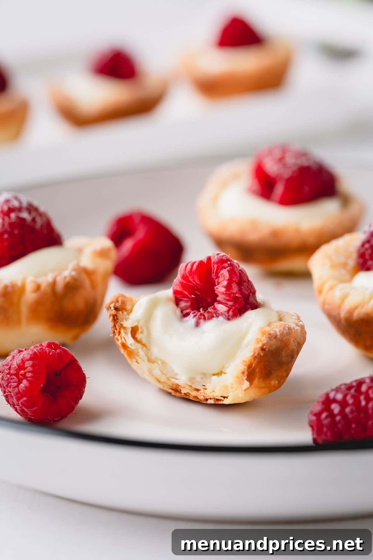 Sun-Kissed Raspberry Lemon Bites 7 A close-up of a raspberry lemon tartlet, with one bitten, revealing the creamy lemon filling and flaky crust.