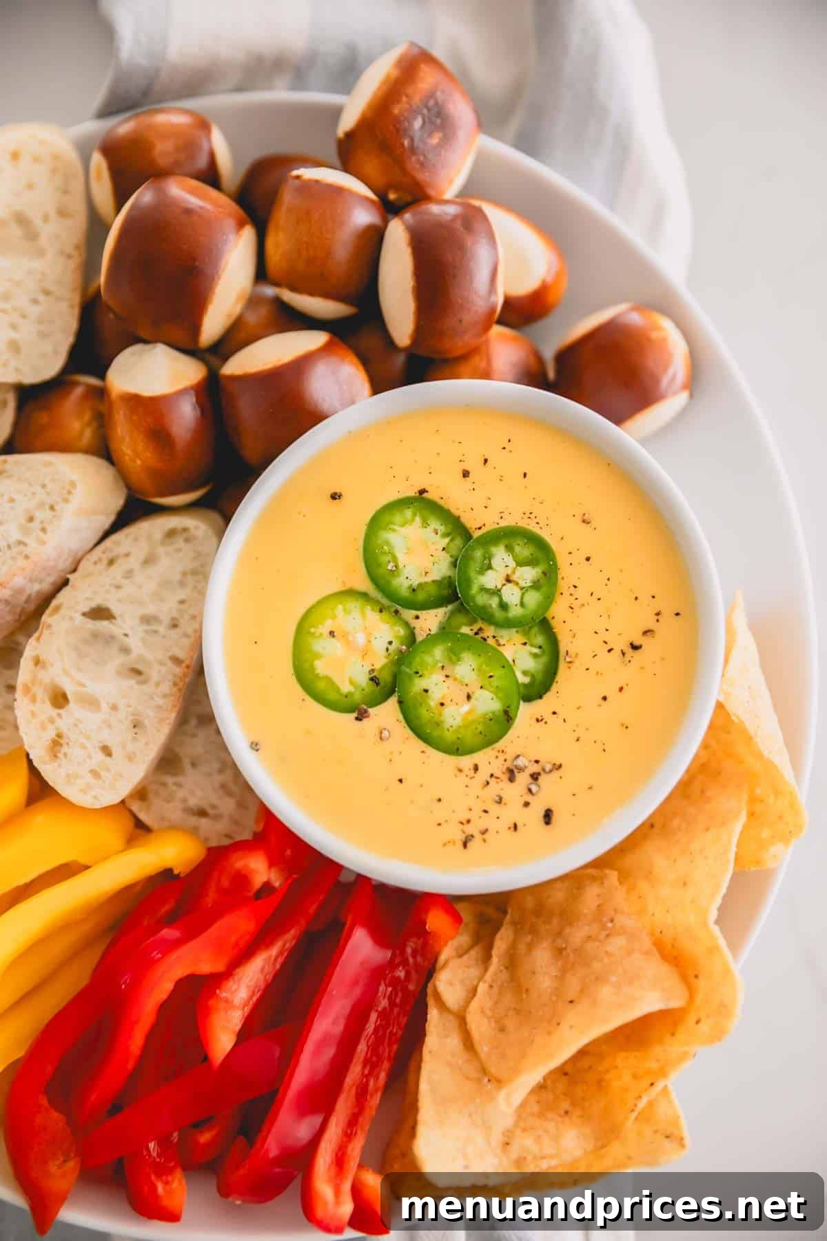 Cheddar Jalapeno Dip 2 Spicy cheddar cheese dip in a white bowl with soft pretzel nuggets, sliced bread, chips, and bell pepper strips.