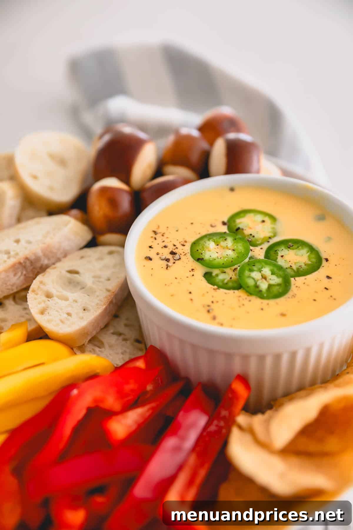 Cheddar Jalapeno Dip 12 A platter with a ramekin of spicy cheddar dip, sliced bread, bell pepper, and pretzel nuggets.