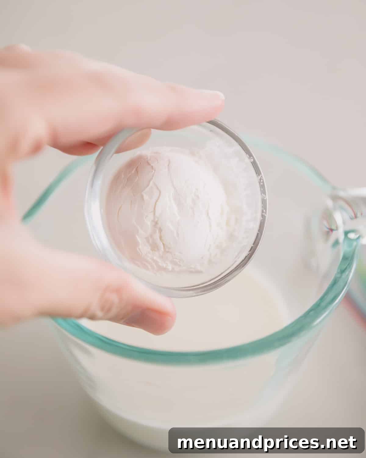 Cheddar Jalapeno Dip 6 A hand adding a small glass bowl of cornstarch to a glass measuring cup of cream.
