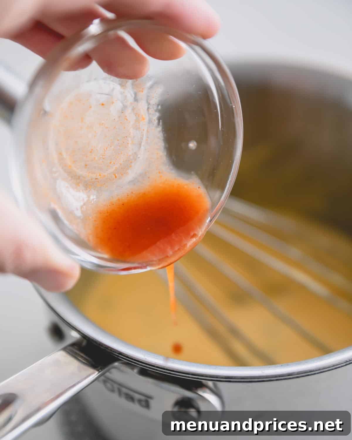 Cheddar Jalapeno Dip 10 A hand adding a small glass bowl of hot sauce.