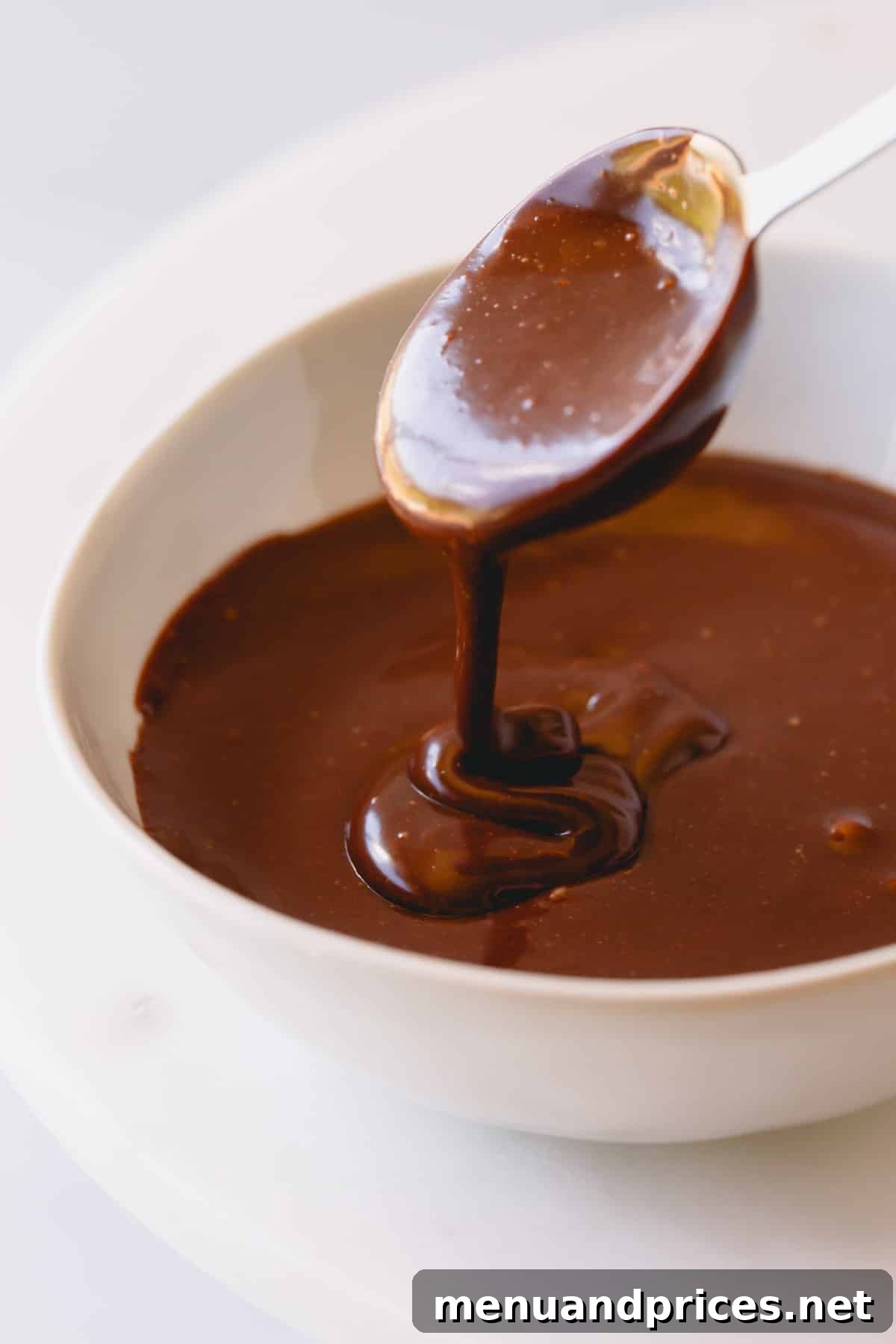 Smooth chocolate frosting in a bowl with a spoon lifting a scoop, showcasing its rich texture.