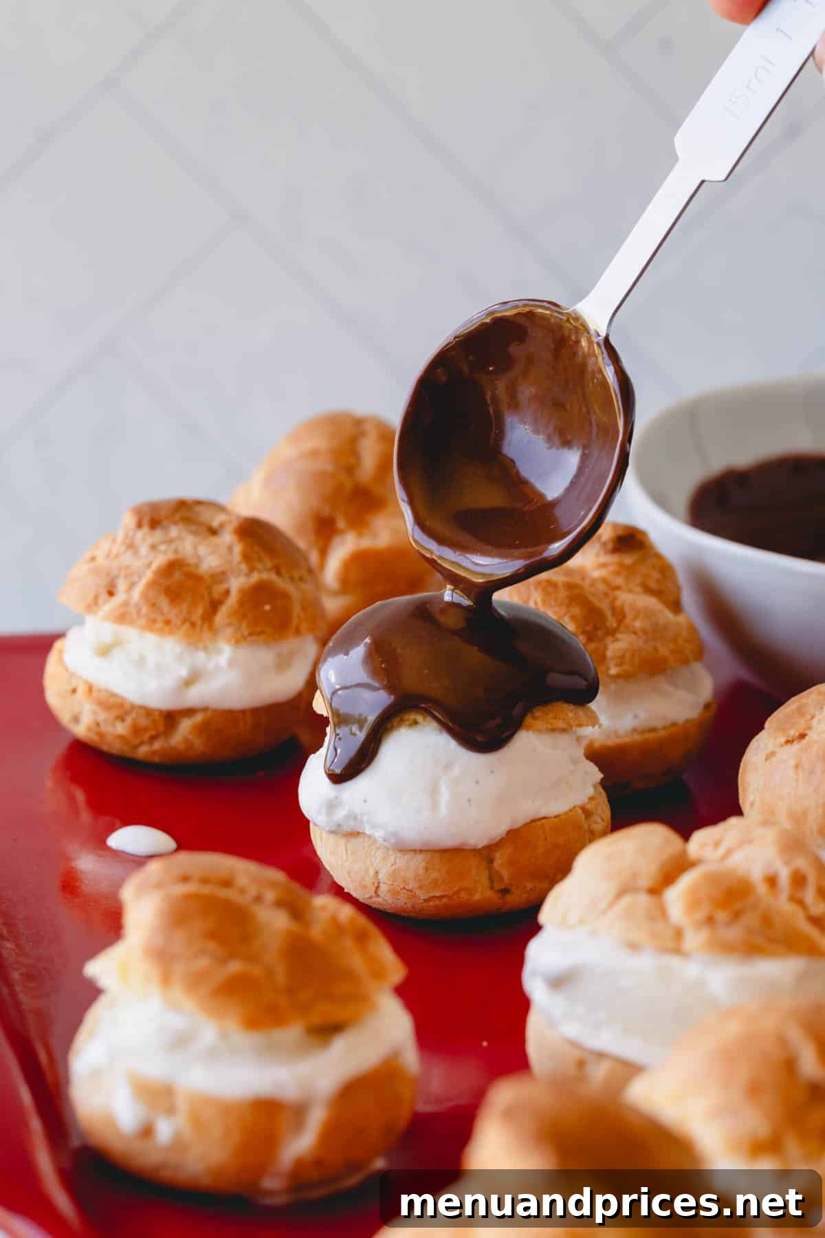 A stream of rich chocolate sauce being poured generously over beautifully arranged profiteroles.