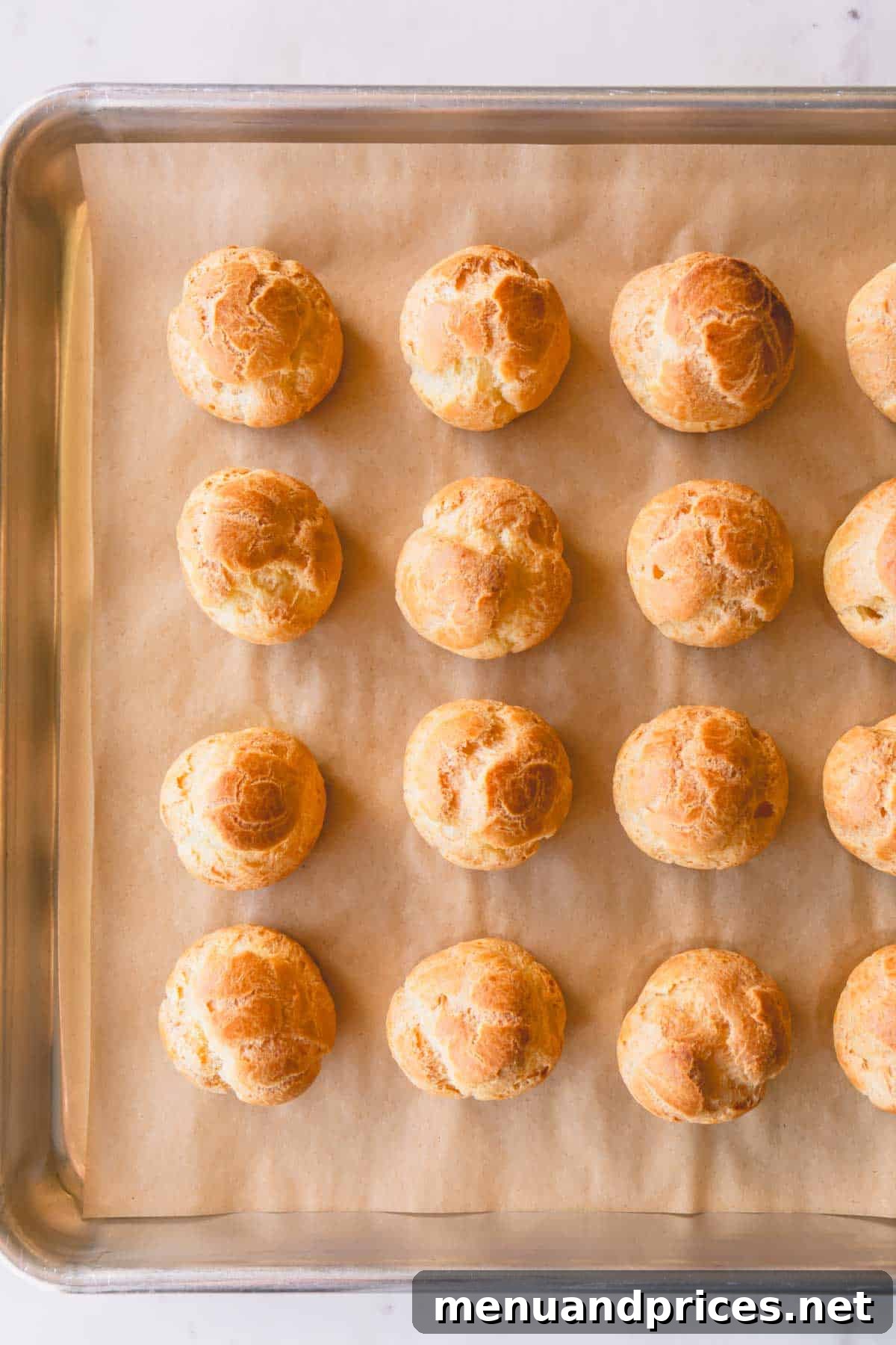 Freshly baked golden-brown profiteroles shells cooling on a baking sheet.