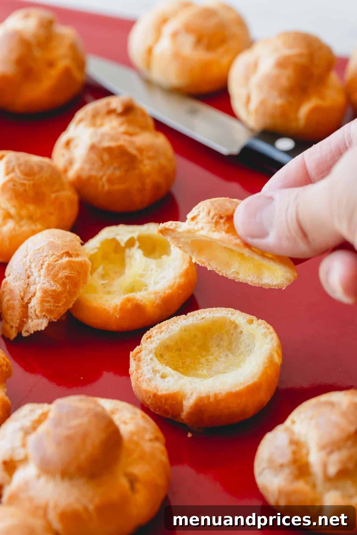 Profiteroles shells being carefully sliced open with a sharp knife, revealing the hollow interior.
