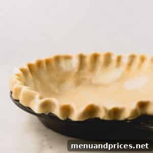 Unbaked pie crust with crimped edges in a black pie dish, ready for baking.