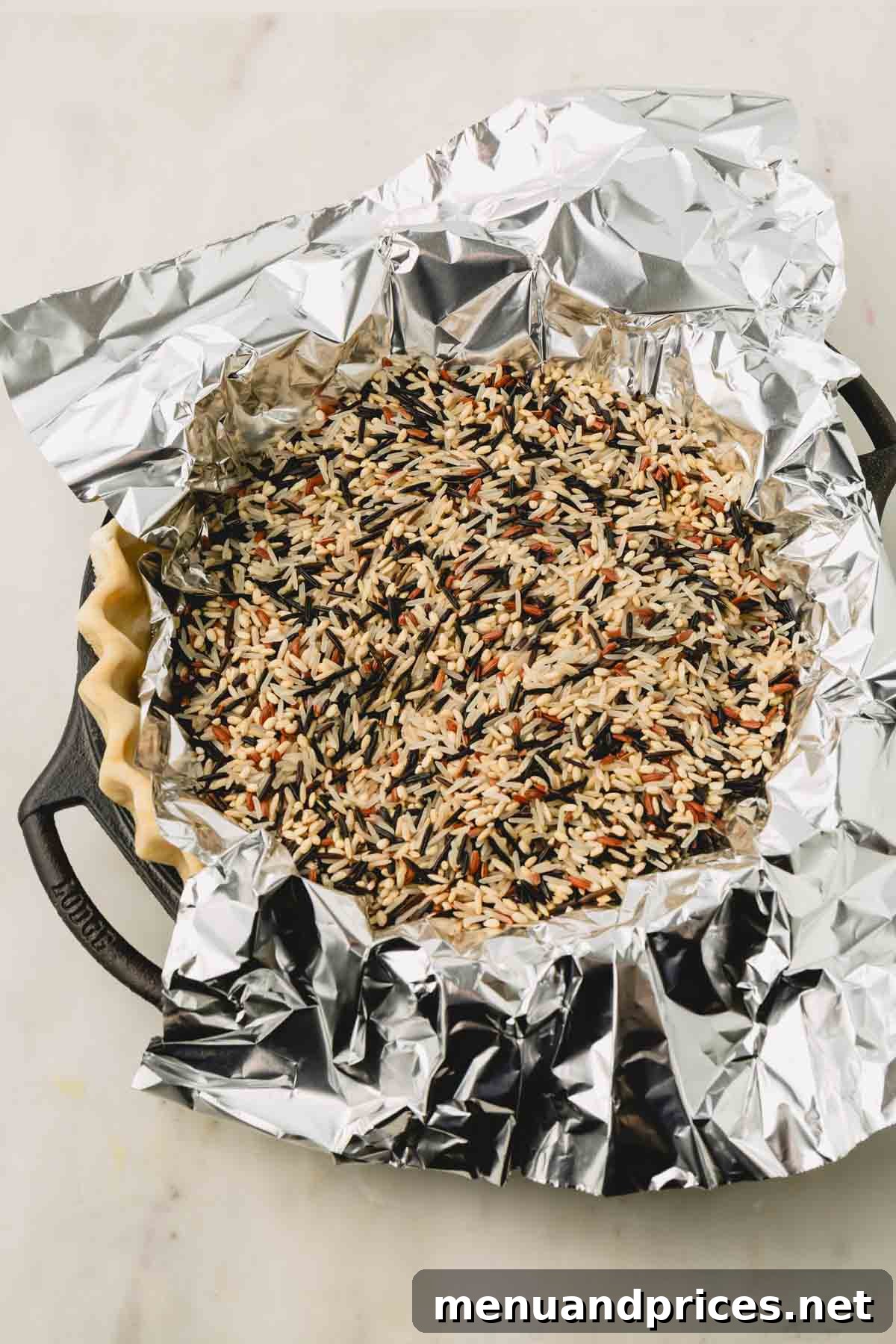 Pure Butter Flaky Pie Pastry 10 A pie crust in a dish, covered with aluminum foil and filled with raw wild rice acting as pie weights, ready for blind baking.