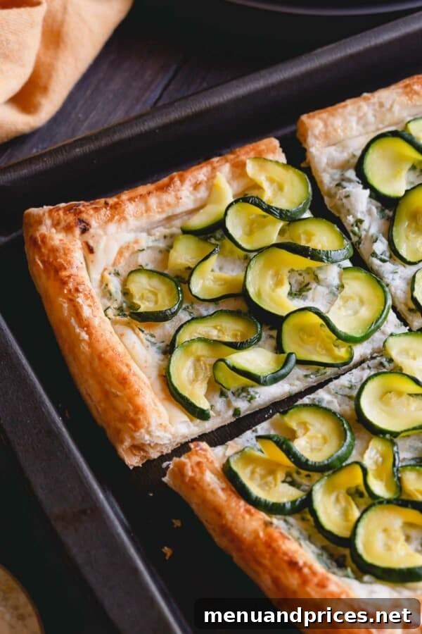 Summer Zucchini Ricotta Tart 2 A close-up shot of a golden-brown zucchini ricotta tart on a baking sheet, showcasing the crispy crust and perfectly arranged zucchini slices.
