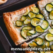 A close-up shot of the zucchini ricotta tart on a baking sheet, with slices.