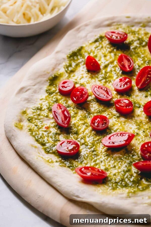 Slow-Roasted Tomato & Golden Mozzarella Pizza 3 Unbaked pesto cherry tomato pizza, beautifully arranged with vibrant green pesto, halved red cherry tomatoes, and shredded mozzarella cheese.