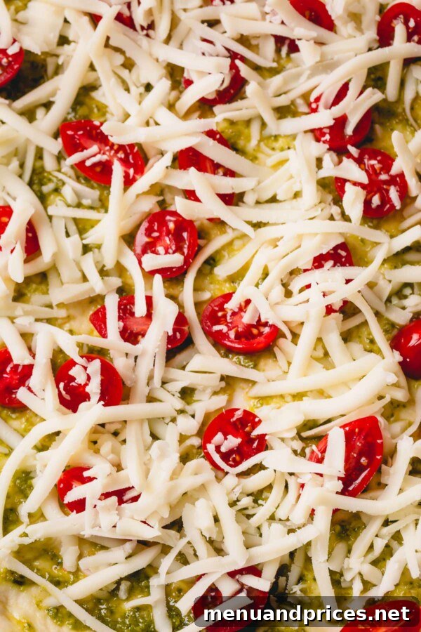 Slow-Roasted Tomato & Golden Mozzarella Pizza 4 Up-close shot of an unbaked pizza with its fresh toppings: aromatic pesto, bright cherry tomatoes, and a generous layer of mozzarella.