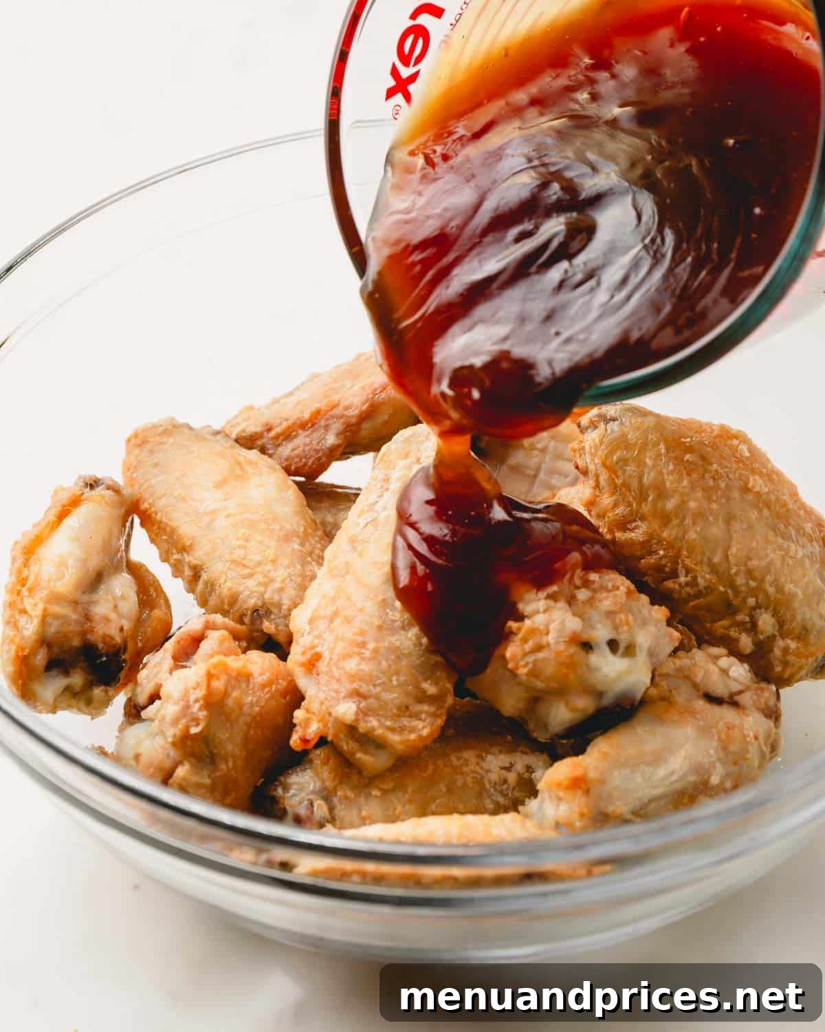 Sticky Teriyaki Chicken Wings 11 Rich, glossy teriyaki sauce being poured generously over a bowl of crispy chicken wings, ready to be tossed and served.