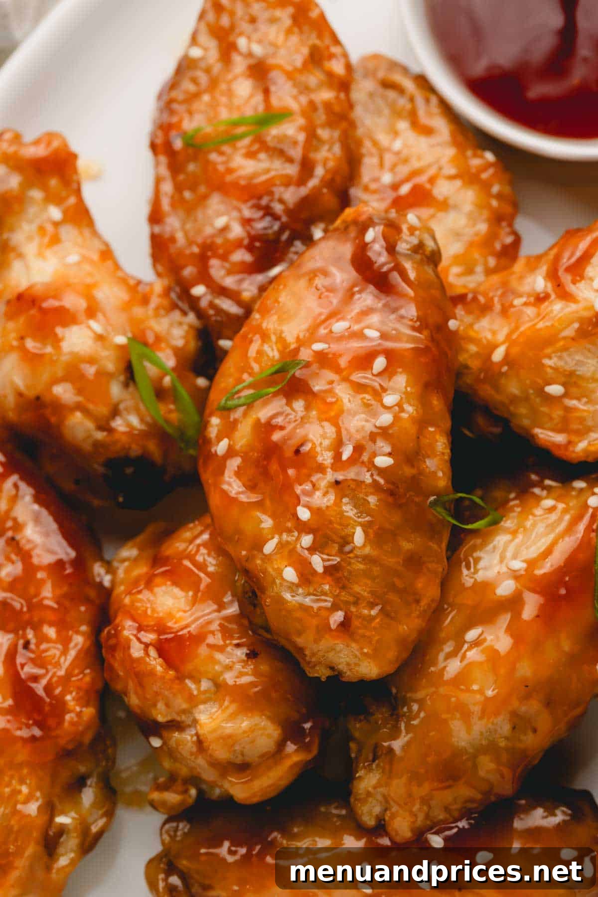 Sticky Teriyaki Chicken Wings 12 A large platter generously filled with oven baked teriyaki chicken wings, beautifully garnished with fresh green scallions and white sesame seeds, ready for a feast.