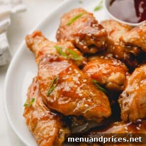 A close-up of a platter of oven baked teriyaki chicken wings topped with scallions and white sesame seeds, ready to be enjoyed.