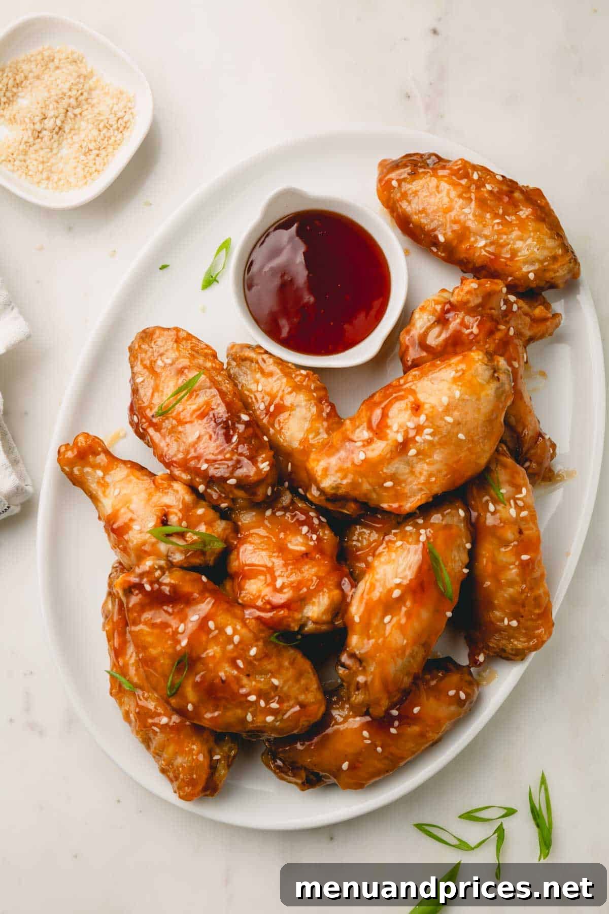Sticky Teriyaki Chicken Wings 3 A close-up shot of a platter filled with perfectly cooked honey teriyaki chicken wings, with a small bowl of extra dipping sauce on the side.