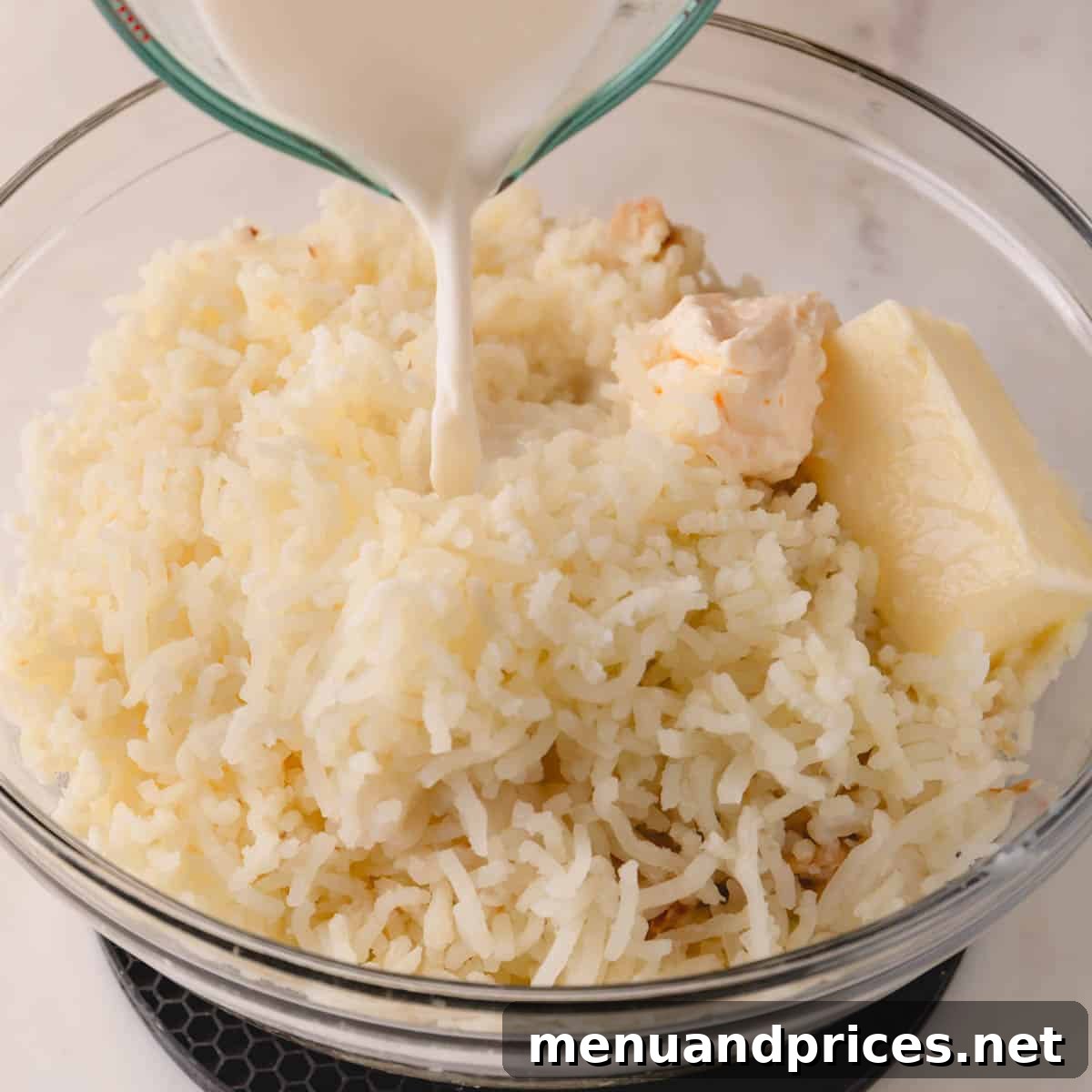 Garlic Infused Potato Perfection 6 A large bowl of riced potatoes with a generous chunk of butter, creamy mayonnaise, and warm milk being poured in.
