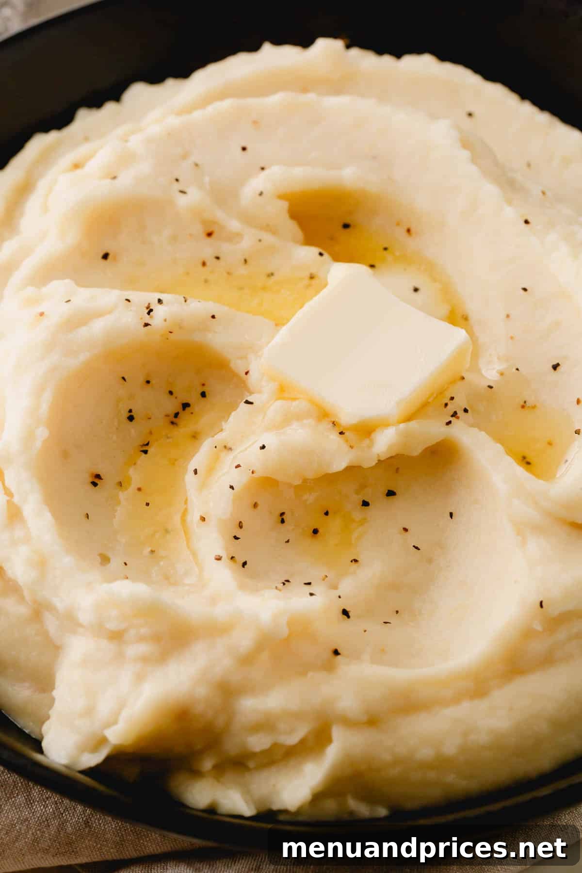 Garlic Infused Potato Perfection 9 A close-up shot of a plate of perfectly smooth roasted garlic mashed potatoes, topped with a dollop of butter and black pepper.