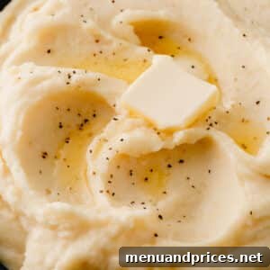 Close up image of a plate of roasted garlic mashed potatoes topped with butter and pepper.