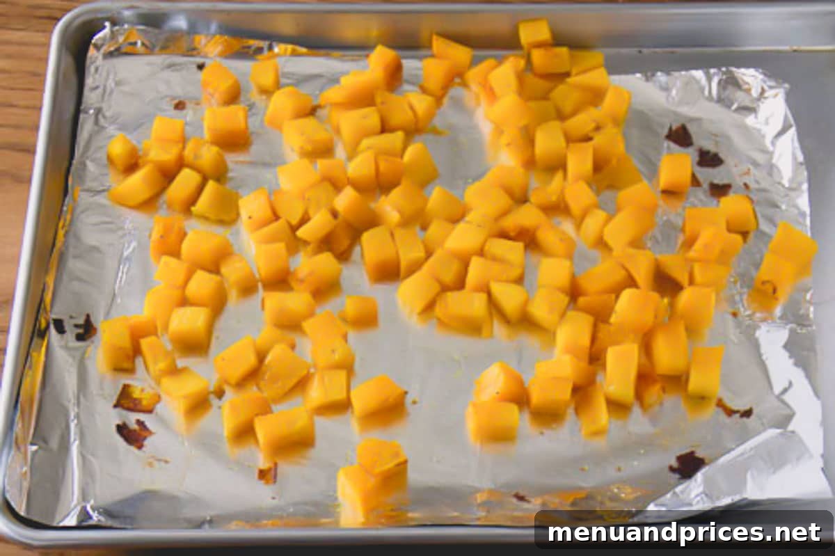 Roasted Brussels Quinoa Harvest Bowl 4 Cubed acorn squash evenly spread on a baking sheet lined with foil, ready for roasting.