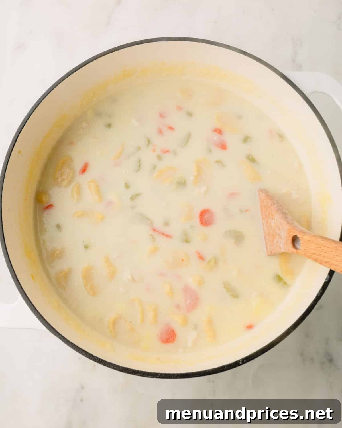 Pillowy Knoephla Noodle Soup 19 A wooden spoon gently stirs the creamy Knoephla soup in a Dutch oven, revealing the cooked dumplings and vegetables.