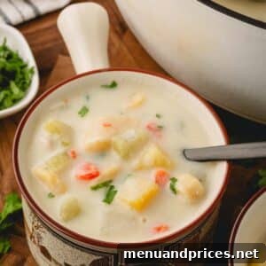 A bowl of Knoephla soup ready to be served, alongside a pot of the soup in the background.