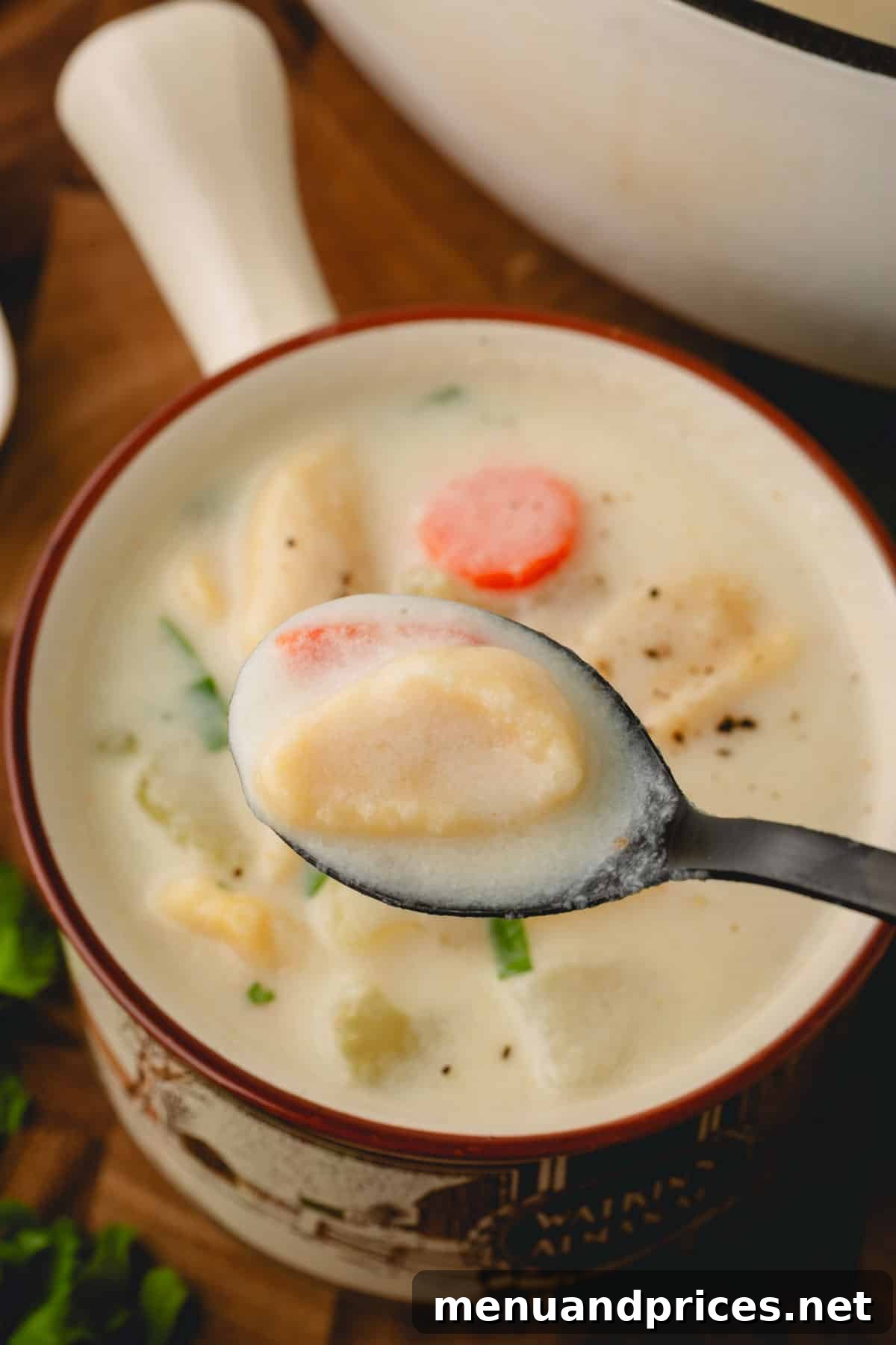 Pillowy Knoephla Noodle Soup 4 A spoonful of Knoephla soup, featuring a dumpling and carrot, held over a bowl of the hearty soup.
